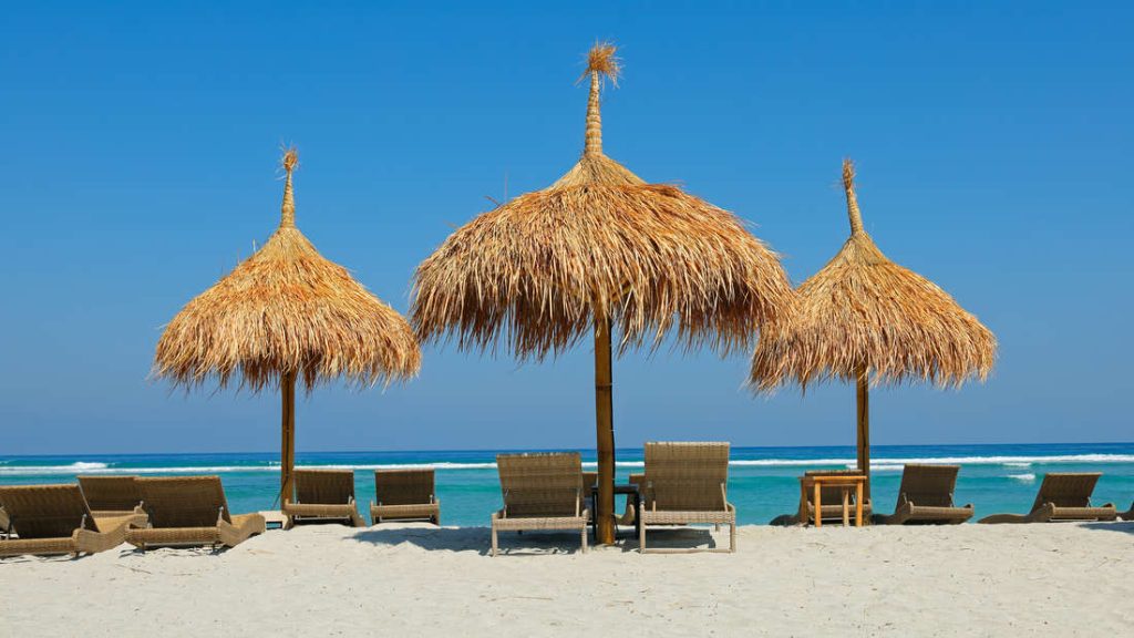 Pantai tropis dengan payung jerami dan kursi geladak di Bali.