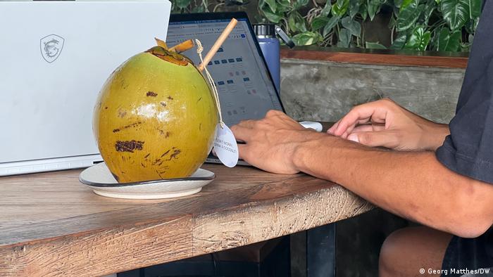 Minuman tropis berdiri di samping komputer laptop yang sedang dikerjakan seseorang, bali
